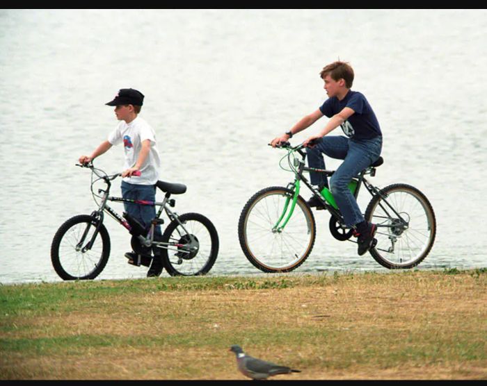 Pangeran William (11 tahun) dan Pangeran Harry (9 tahun) bersepeda bersama.