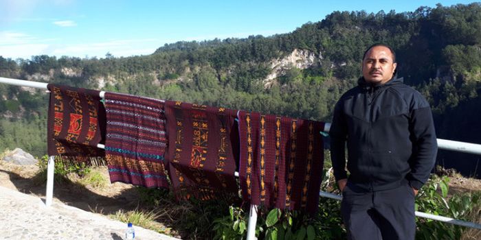Imran Nahumarury berpose di samping kain-kain hasil tenunan penduduk setempat yang dijual di puncak 