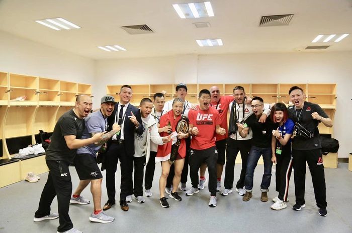 Juara UFC pertama asal China, Zhang Weili, berpose bersama timnya usai kemenangan kontra Jessica Andrade pada UFC Shenzhen, Sabtu (31/8/2019).