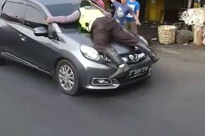 Seorang polisi berusaha menghentikan mobil yang kabur dari razia.