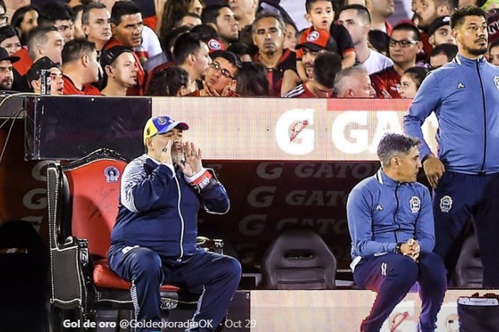 Legenda sepak bola Argentina yang kini melatih Gimnasia La Plata, Diego Maradona, duduk di atas kursi spesial ketika menemani timnya berlaga melawan Newell's Old Boys, Rabu (30/10/2019) di Stadion Marcelo Bielsa.