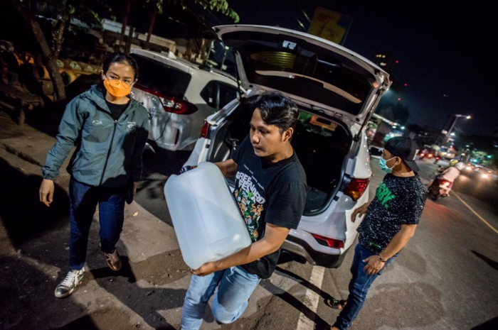 Ivo Ananda (kiri) dibantu tim Bonek Disaster Response Team untuk menurunkan cairan disinfektan. Ivo memberikan bantuan kepada BDRT sebanyak 250 liter cairan disinfektan.