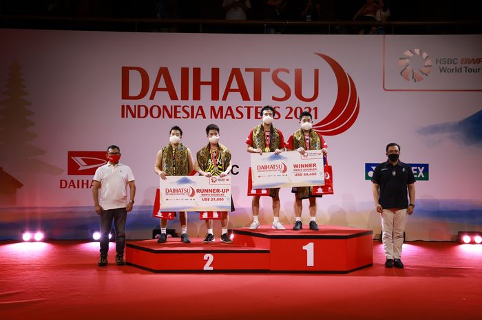 Marcus Fernaldi Gideon/Kevin Sanjaya Sukamuljo (jersey kuning) dan Takuro Hoki/Yugo Kobayashi berbaris di podium setelah final Indonesia Masters 2021 di Bali International Convention Centre, Nusa Dua, Bali, 21 November 2021.