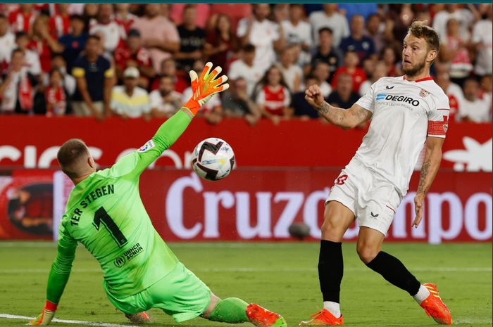 Aksi kiper Barcelona, Marc-Andre ter Stegen, mencegat bola dari gelandang Sevilla yang juga eks rekannya, Ivan Rakitic di Stadion Ramon Sanchez Pizjuan, Minggu (4/9/2022) dini hari WIB.