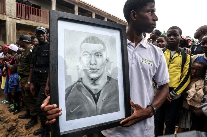 Seorang warga memegang potret striker PSG, Kylian Mbappe, di area sekolah Bonendale, yang dibangun oleh yayasan milik sang bomber di Douala, Kamerun (8/7/2023). Mbappe ditawari gaji 11,6 triliun agar mau pindah ke Al Hilal di bursa transfer musim panas 2023.