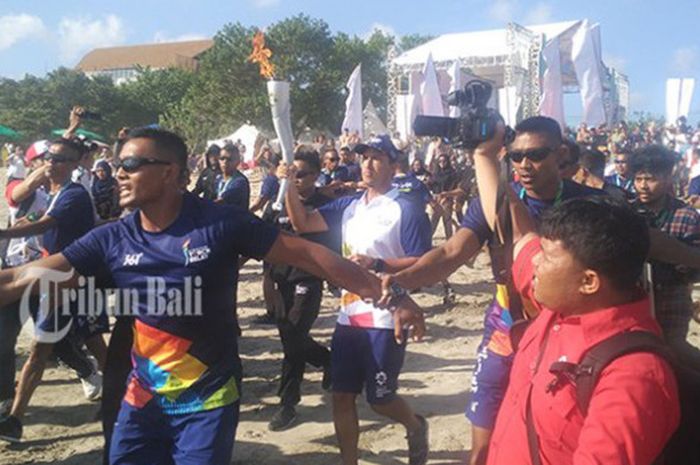 Aktor Hamish Daud (baju putih) membawa obor Asian Games 2018 menuju bibir laut di Pantai Kuta, Bali, sebelum membawanya berselancar pada Senin (23/7/2018).