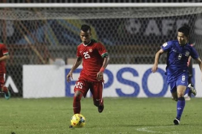 Pemain bertahan Indonesia, Manahati Lestusen membawa bola menjauh dari gelandang Thailand, Sarach Yooyen.