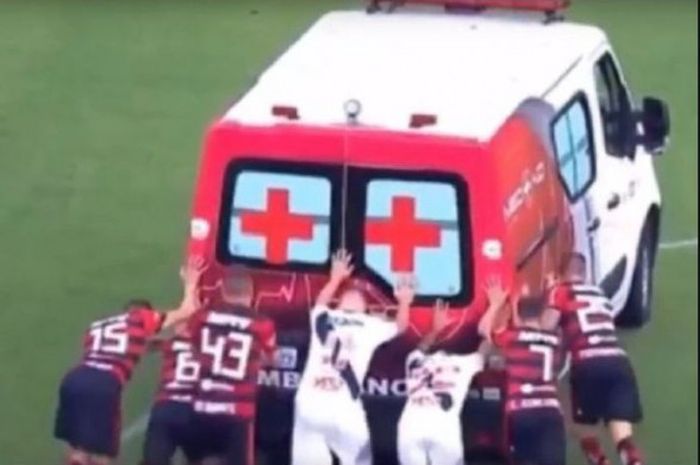Pemain klub Liga Brasil bahu membahu mendorong mobil ambulans yang mogok di lapangan.