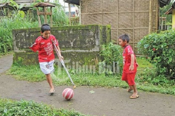 I Putu Ari Krisna Saputra yang biasa dipanggil Yoko sedang menunjukkan kemampuannya menendang bola saat bermain dengan adiknya di sekitar kediaman mereka di Banjar Dinas Petung, Batur Tengah, Kintamani, Bangli, Bali Kamis (15/2/2018). 