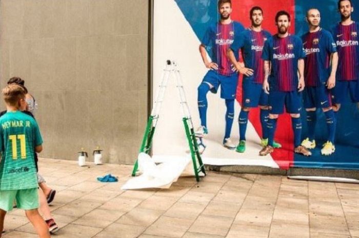 Seorang penggemar Barcelona yang memakai jersey Neymar melintasi poster yang sudah tak lagi ada sang pemain Brasil tersebut.