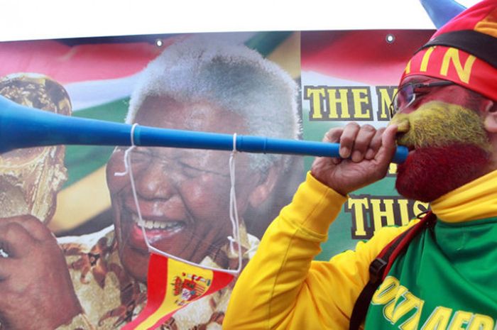 Seorang penonton Piala Dunia 2010 meniup terompet khas Afrika Selatan, vuvuzela, di depan foto Nelson Mandela di luar Stadion Moses Mabhida, Durban, pada 7 Juli 2010.
