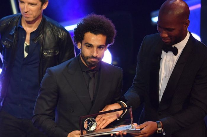 Penyerang Liverpool, Mohamed Salah (tengah), saat menerima trofi Puskas Award dari eks striker asal Pantai Gading, Didier Drogba (kanan), dan musisi Inggris, Noel Gallagher, dalam acara FIFA The Best 2018 di Royal Festival Hall, London, Inggris, pada Senin (24/9/2018).