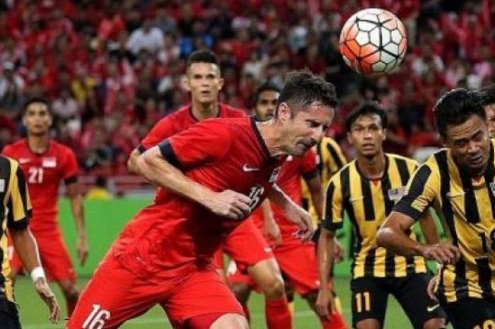 Bek Singapura, Daniel Bennett (merah) menyundul bola untuk menjauhkan dari penyerang Malaysia, Hazwan Bakri di Stadion Nasional, Jumat (7/10/2016) malam.  