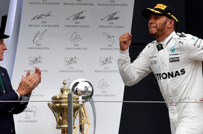 Legenda Formula 1 (F1) asal Inggris, Sir Jackie Stewart (kiri), memberi aplaus kepada pebalap Mercedes dari Inggris, Lewis Hamilton, saat tiba di atas podium juara GP Inggris di Sirkuit Silverstone, Minggu (16/7/2017).