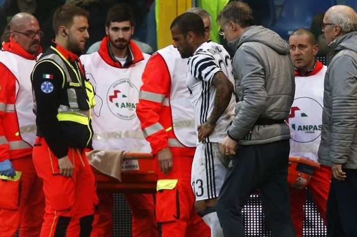 Bek kanan Juventus, Dani Alves, berjalan meninggalkan lapangan sambil didampingi oleh tim medis di Stadion Luigi Ferraris, Minggu (27/11/2016).