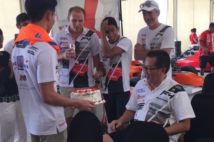 Pebalap Indonesia, Perry Martono, menyerahkan kue ulang tahun untuk sang ayah, Perry Martono (duduk), di sela-sela sesi latihan seri keenam Formula 4 South East Asia (F4 SEA) di Sirkuit Sepang, Malaysia, Jumat (20/1/2017).