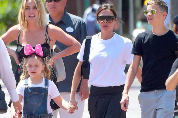 Harper Beckham (kiri) memakai bando minnie mouse merah jambu bersama Victoria Beckham (tengah) memakai kacamata hitam dan Romeo Beckham (kanan) memakai kacamata saat di Disneyland, Sabtu (14/4/2018)