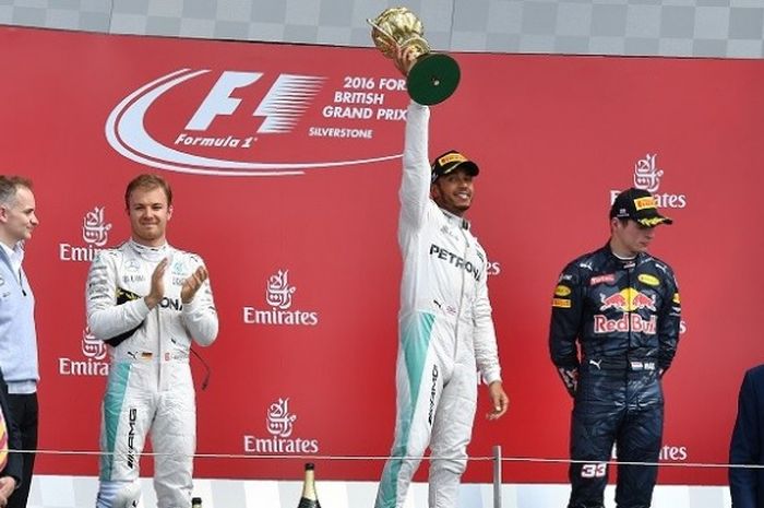 Pebalap Mercedes, Lewis Hamilton, mengangkat trofi juara di podium setelah memenangi GP Inggris di Sirkuit Silverstone, Minggu (10/7/2016).