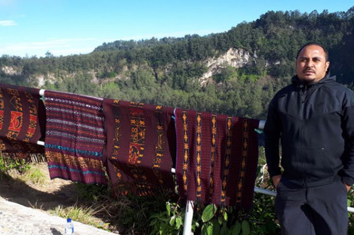 Imran Nahumarury berpose di samping kain-kain hasil tenunan penduduk setempat yang dijual di puncak Gunung Kelimutu, Senin (24/7/2017).