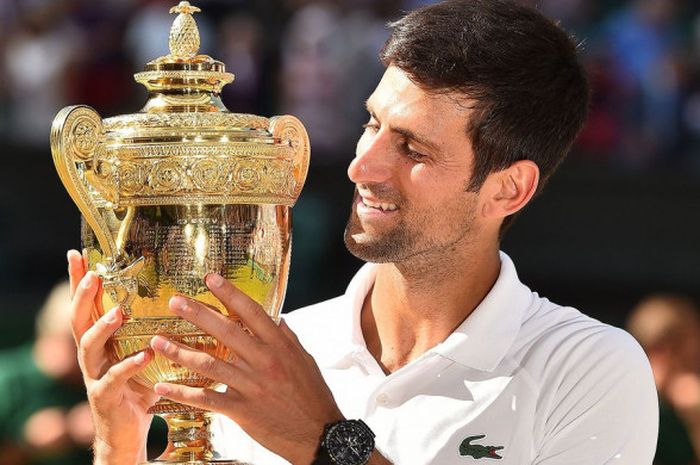 Novak Djokovic (Serbia) tersenyum saat memegangi piala Wimbledon 2018 usai memenangi partai final yang digelar Minggu (15/7/2018).