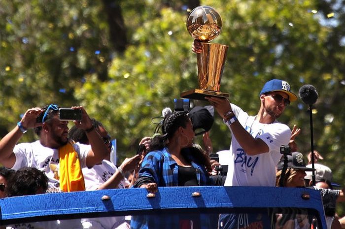 Pebasket bintang Golden State Warriors, Stephen Curry, mengangkat trofi Larry O'Brien yang diraih setelah memenangi seri final pada parade juara NBA 2018 di Kota Oakland, California, Amerika Serikat, Selasa (12/6/2018) siang waktu setempat.