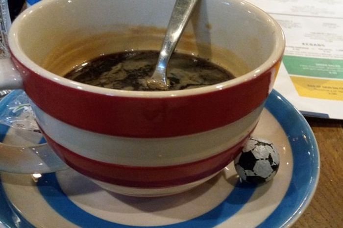 Secangkir kopi Americano di Cafe Football disajikan dengan sebutir cokelat berbentuk bola sepak. 