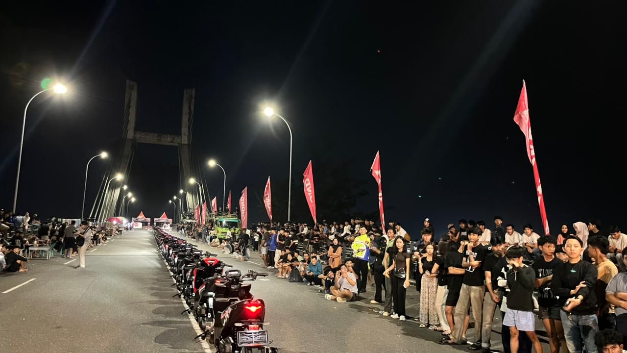 Motor berjejer di tengah garis jalan yang dengan kumpulan warga yang melihat dari sisi kiri dan kanan
