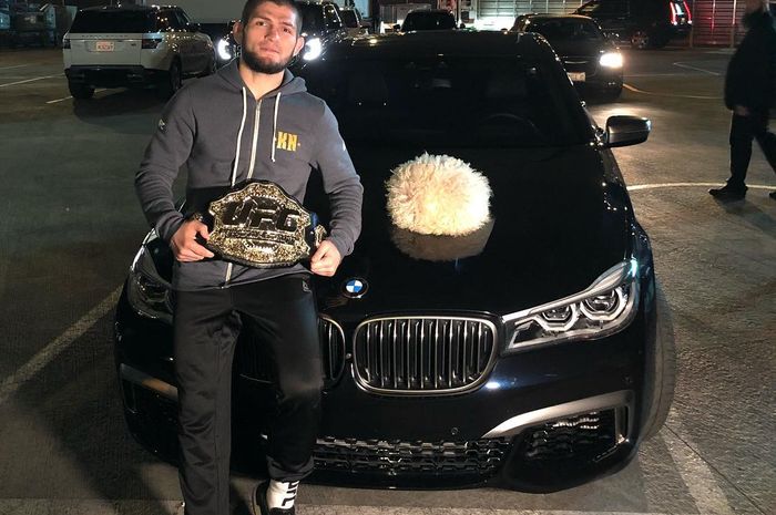 Khabib Nurmagomedov berpose dengan sabuk kemenangan di depan sebuah mobil