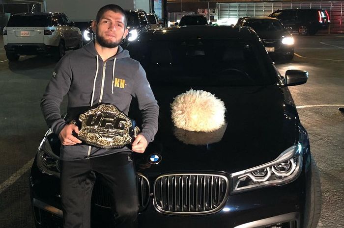 Khabib Nurmagomedov berpose dengan sabuk kemenangan di depan sebuah mobil