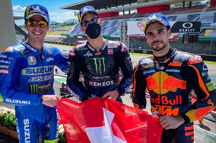 Para penghuni podium MotoGP Italia 2021 (dari kiri ke kanan): Joan Mir, Fabio Quartararo, dan Miguel Oliveira berpose dengan bendera Swiss untuk mengenang mendiang pembalap Moto3, Jason Dupasquier, yang meninggal dunia usai mengalami kecelakaan pada sesi kualifikasi Moto3 Italia 2021.