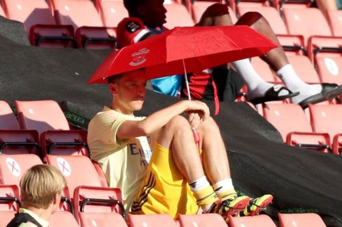Mesut Oezil menyaksikan laga Arsenal dari bangku penonton dengan memakai payung.