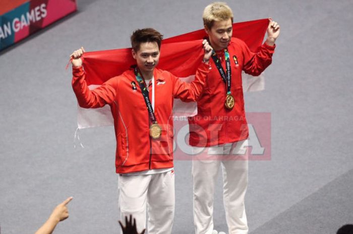 Marcus Fernaldi Gideon (kanan) dan Kevin Sanjaya Sukamuljo (kiri) membentangkan bendera Merah Putih seusai menjuarai nomor ganda putra pada Asian Games 2018.